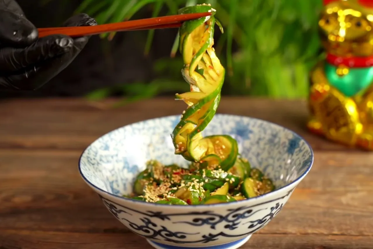 Chrupiące og&oacute;rki po tajsku, doprawione sezamem i chili, podniesione pałeczkami z miseczki.