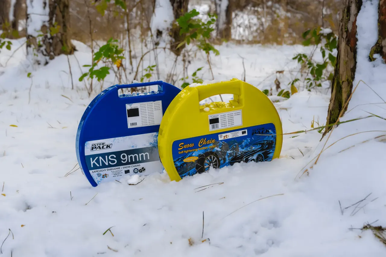Dwa opakowania łańcuch&oacute;w śniegowych w śniegu. Przygotuj się na zimę, by uniknąć mandatu za brak łańcuch&oacute;w w Polsce.