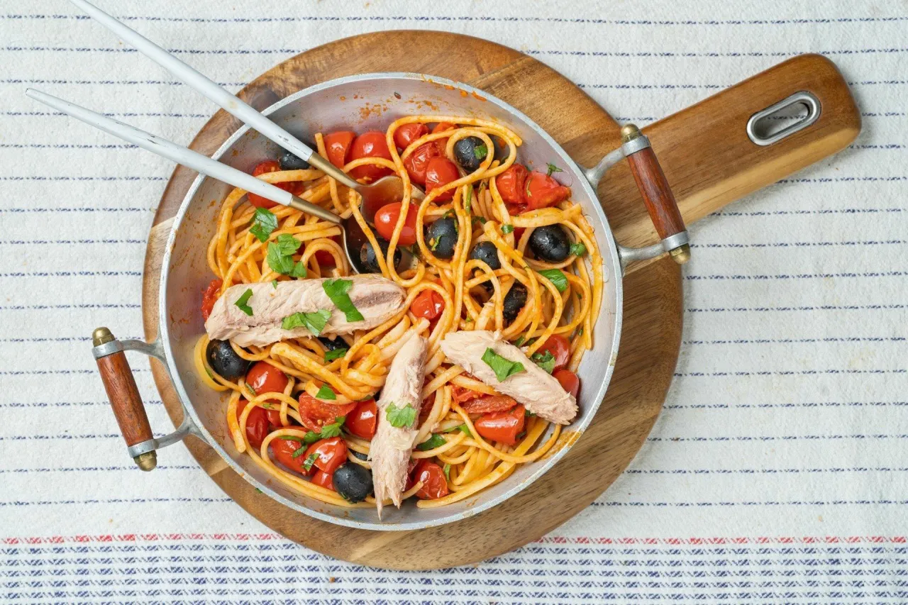 Spaghetti Puttanesca przepis: makaron z pomidorkami, czarnymi oliwkami i tuńczykiem, udekorowany natką pietruszki.