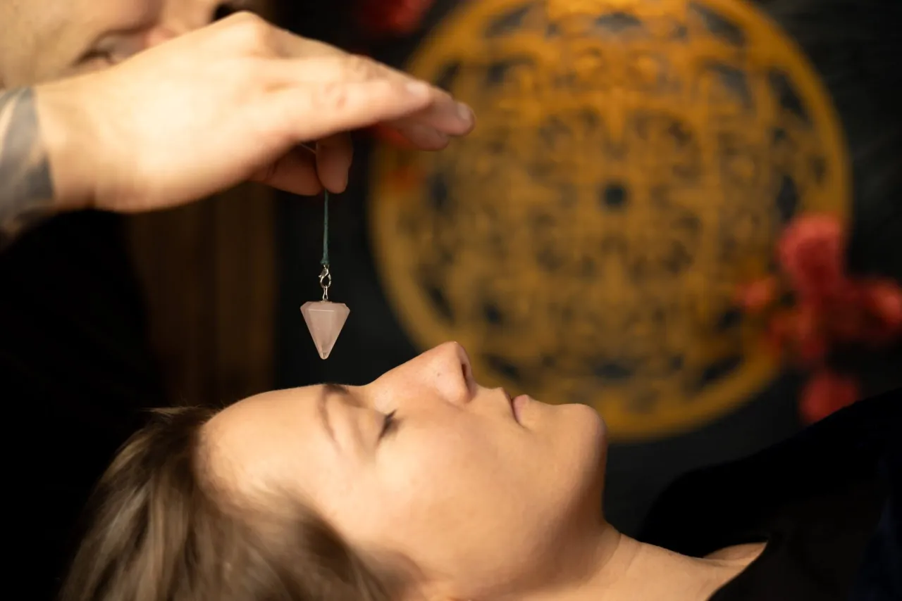 Dłoń trzyma wahadełko nad twarzą kobiety, sugerując pracę z energią i pytając, co to są czakry u człowieka.