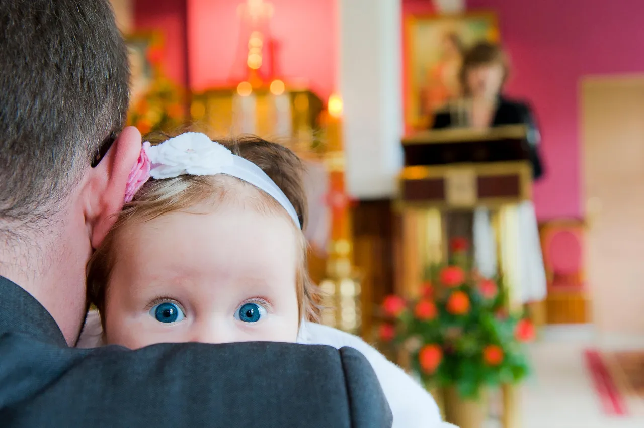 Malutkie dziecko z niebieskimi oczami ukrywa się za ramieniem ojca podczas chrzcin. Zastanawiasz się, ile bierze fotograf za chrzciny?
