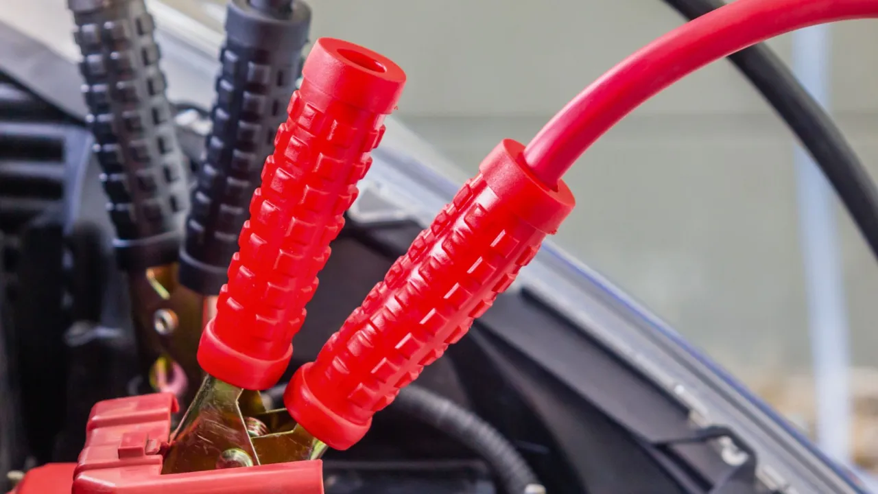 Czerwone i czarne kable rozruchowe podłączone do akumulatora. Dowiedz się, jak podłączyć kable rozruchowe, aby uruchomić samoch&oacute;d.