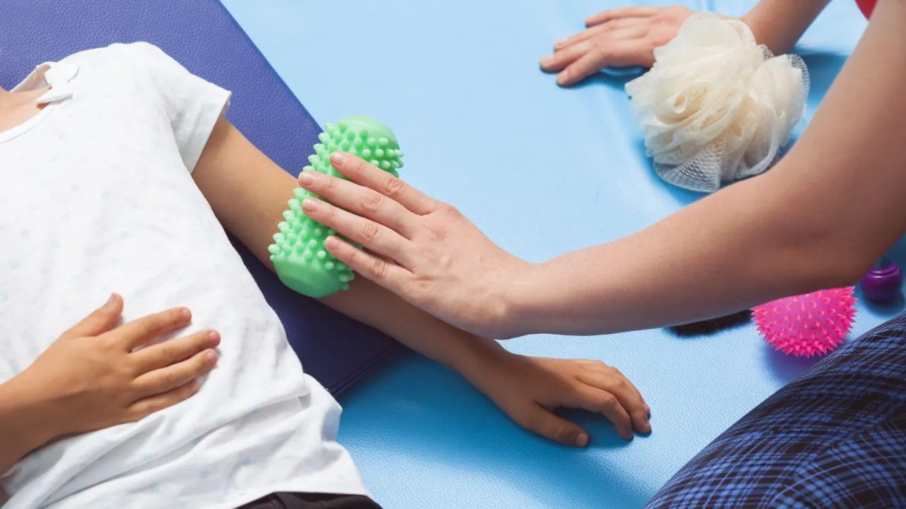 Terapia integracji sensorycznej: dziecko otrzymuje masaż kolczastym wałkiem. Dowiedz się, jak zostać terapeutą integracji sensorycznej.