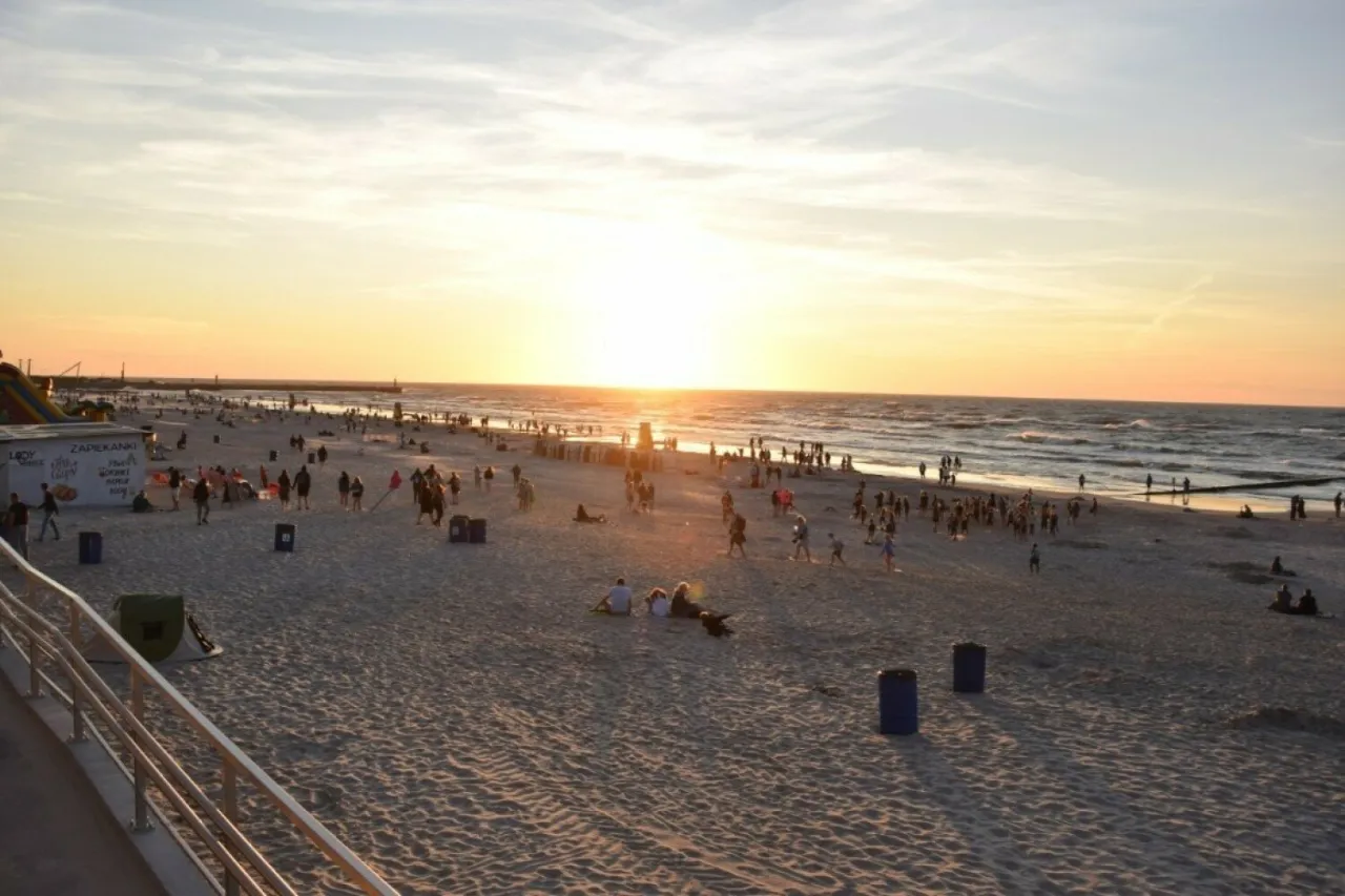 Zachód słońca na plaży w Łebie, gdzie tłumy ludzi cieszą się wieczorem. Choć nie znamy dokładnej liczby mieszkańców Łeby, to widać, że miasto tętni życiem.