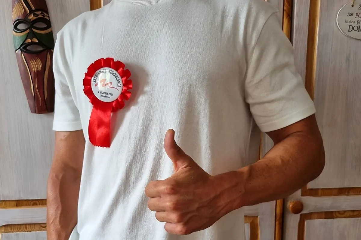 Czerwony kotylion przypięty do białej bluzki, z napisem 