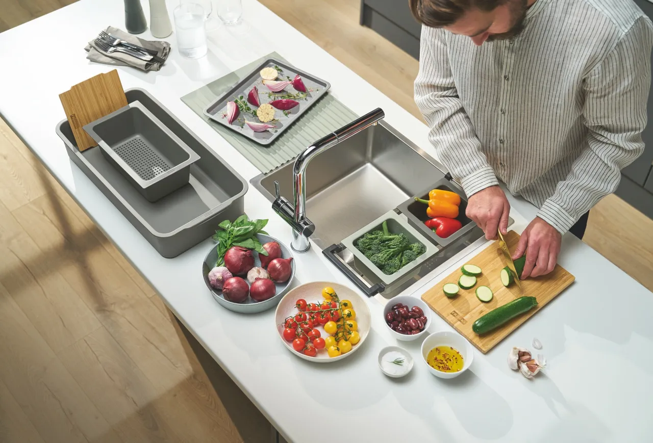 Mężczyzna kroi cukinię przy zlewie, otoczony świeżymi warzywami i akcesoriami do zlewozmywaka.