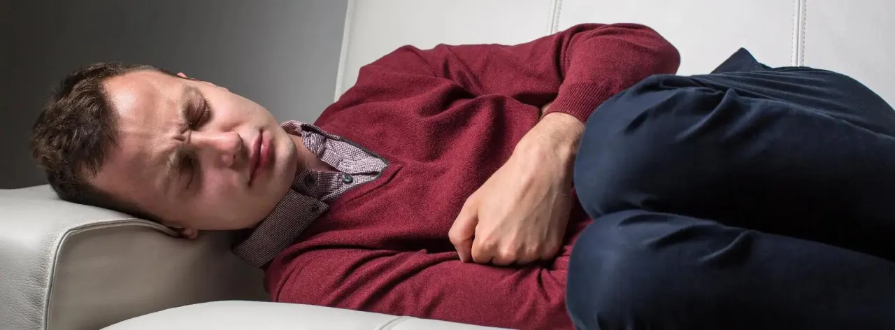 Osoba odczuwająca zmęczenie, trzymająca się za głowę, z bólem brzucha