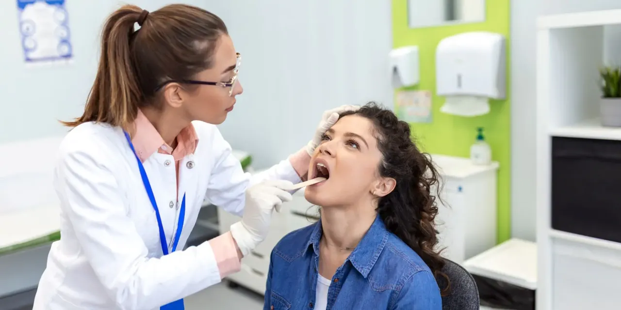 Lekarz bada gardło pacjentki, szukając przyczyn b&oacute;lu gardła.