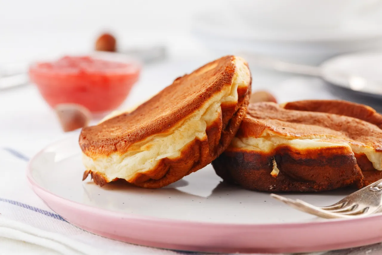 Puszyste placuszki z banan&oacute;w fit na talerzu, obok miseczka z musem truskawkowym. Idealne na zdrowe śniadanie.