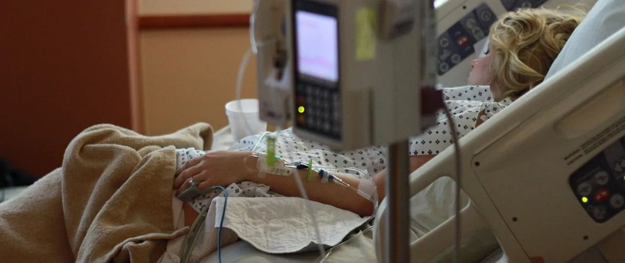 Pacjentka w ł&oacute;żku szpitalnym, z kropl&oacute;wką i aparaturą medyczną, symbolizująca zakończenie leczenia i powr&oacute;t do zdrowia.