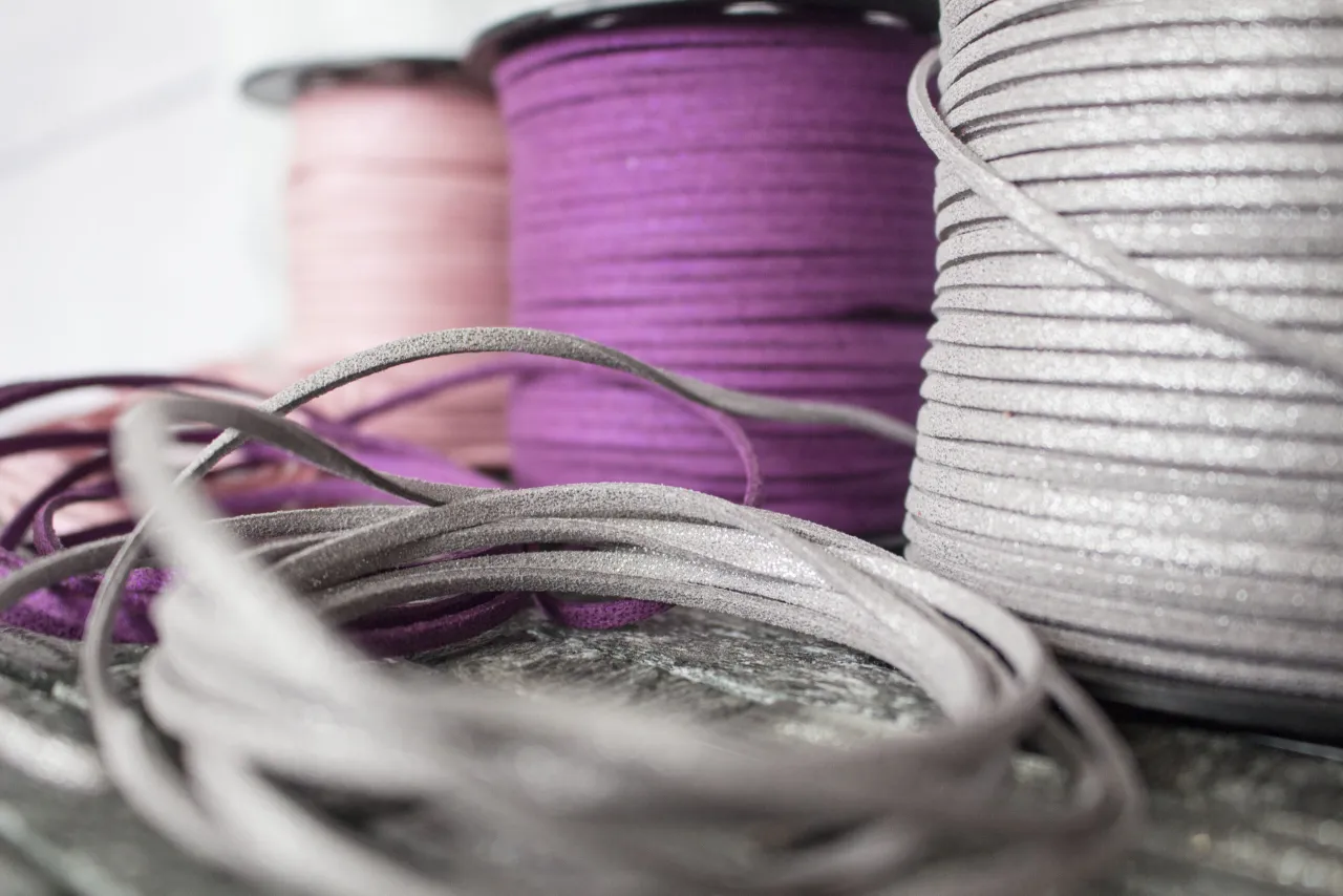 Srebrny, fioletowy i różowy rzemień do wiązania, zwinięty na szpulach, tworzy piękne tło dla luźno leżących, szarych sznurków.