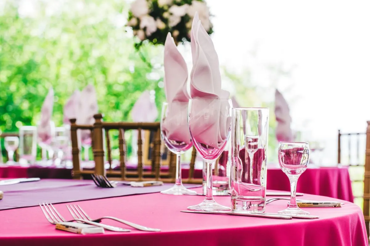 Stół nakryty na obiad weselny zamiast wesela. Różowe obrusy, szkło i sztućce czekają na gości.