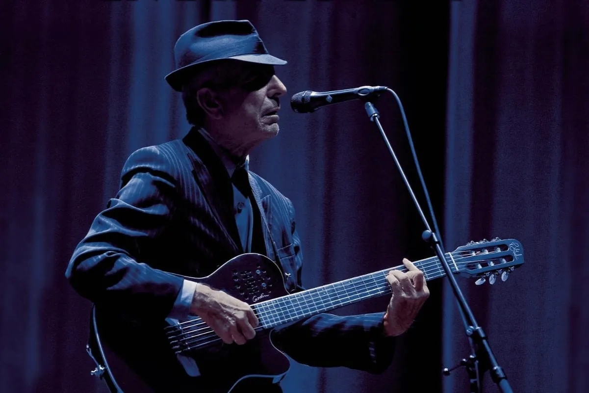 Mężczyzna w kapeluszu gra na gitarze i śpiewa do mikrofonu. Alleluja, jaka to melodia, kt&oacute;ra porusza serca!