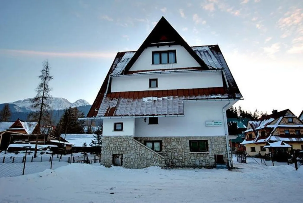Zimowy krajobraz w Zakopanem. Biały budynek z kamienną podstawą i rudym dachem, otoczony śniegiem. W tle g&oacute;ry. Zastanawiasz się, ile kosztuje nocleg w Zakopanem?
