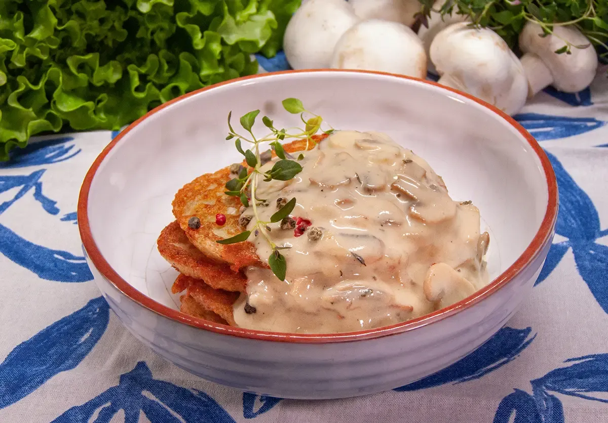 Placki ziemniaczane z kremowym sosem pieczarkowym, ozdobione gałązką tymianku. Idealny pomysł, co dodać do sosu pieczarkowego, by był pyszny.