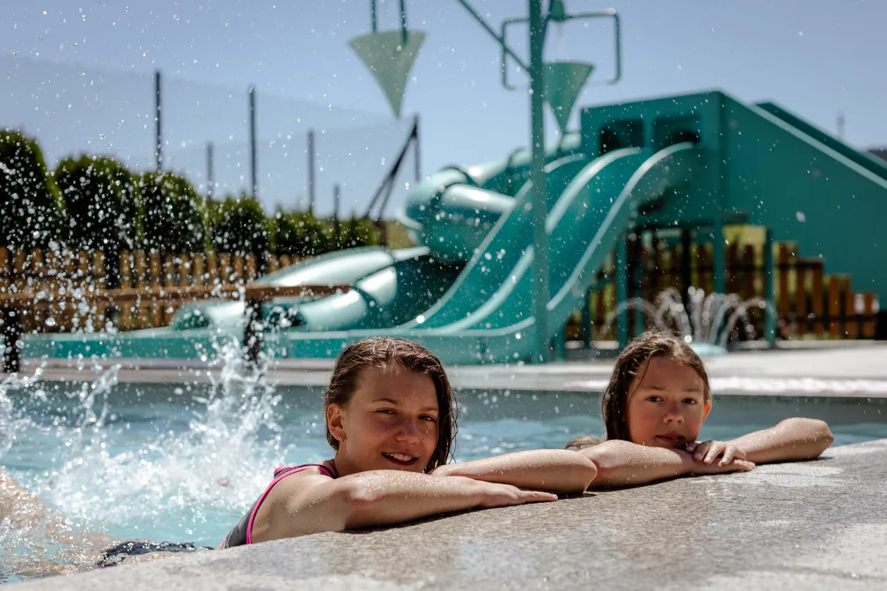 Dwie dziewczynki w basenie, w tle zjeżdżalnie wodne. To byłby wspaniały sylwester z dziećmi, pełen radości i wodnych zabaw!
