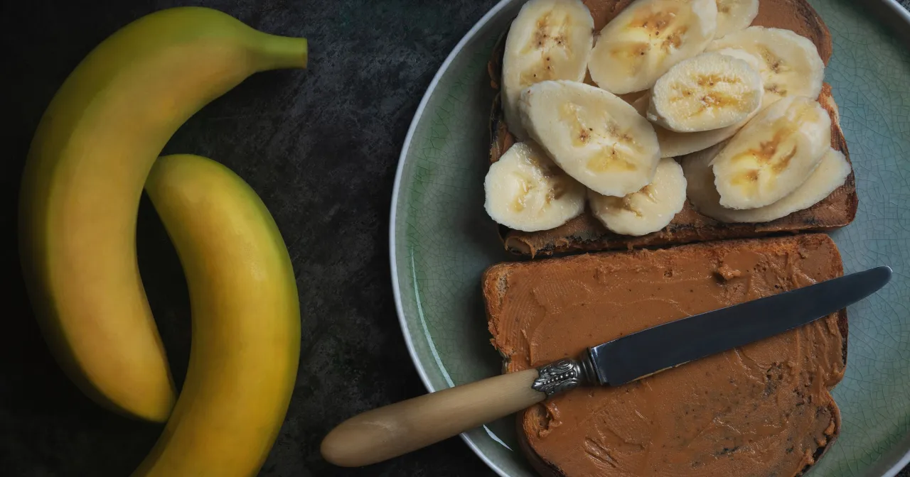 Dwa tosty z masłem orzechowym i bananem, idealne na szybkie i zdrowe przepisy na zdrową kolację. Obok leżą dwa ż&oacute;łte banany.