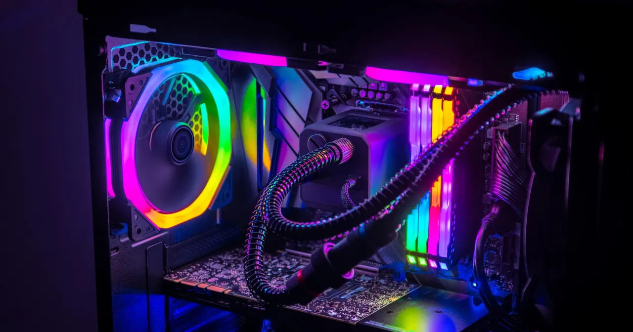 Wnętrze komputera z kolorowym podświetleniem RGB. Widoczne części komputera: wentylator, chłodzenie wodne, RAM, płyta główna.