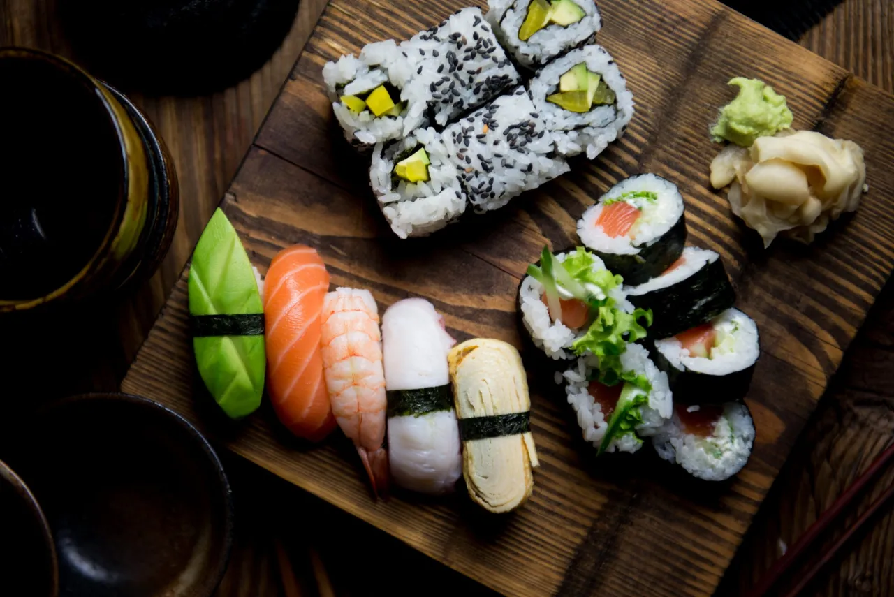 Uramaki sushi z awokado i czarnym sezamem, obok nigiri z łososiem, krewetką i omletem.