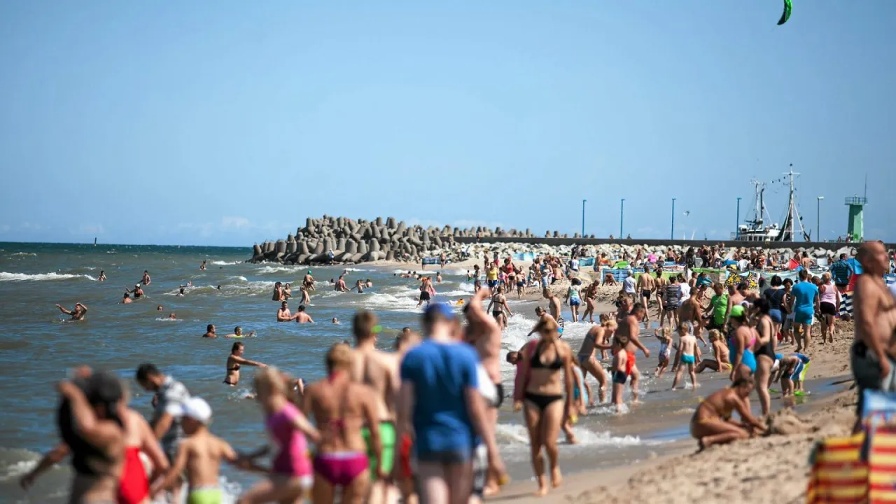Tłum ludzi na plaży i w wodzie. W tle falochron i port. Idealne miejsce, by sprawdzić, gdzie jest najcieplejsze morze w Polsce.