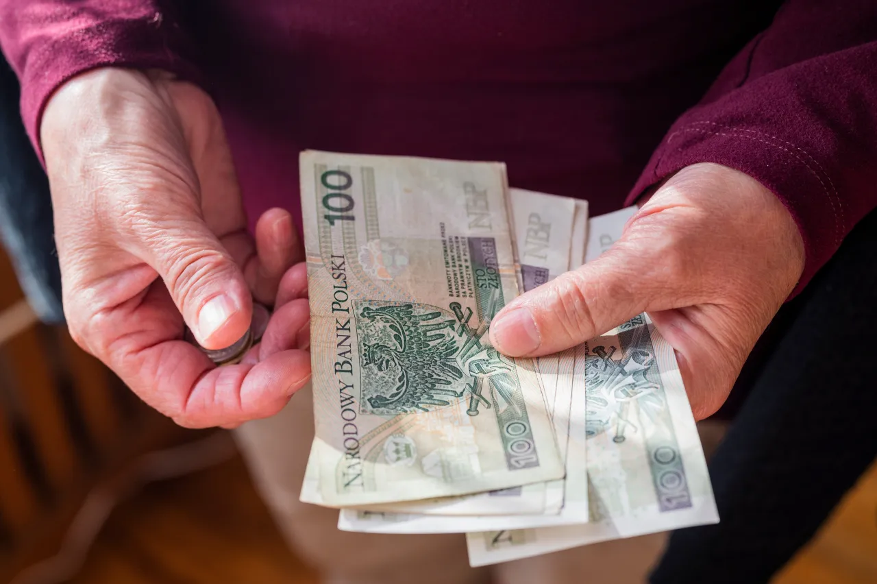 Dłonie trzymają polskie banknoty 100 zł. Czy to już czas na 14. emeryturę i dla kogo?