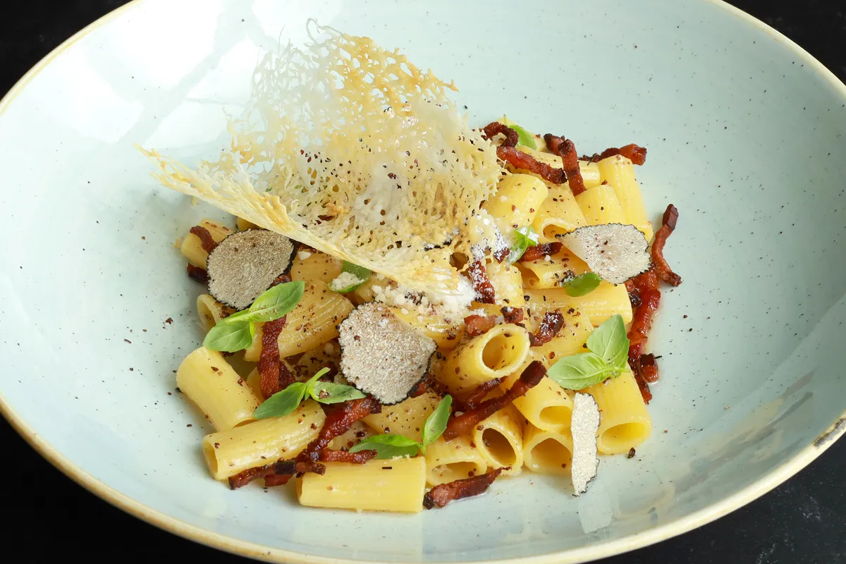Pyszne danie z makaronem rigatoni, chrupiącym guanciale, czarną truflą i listkami bazylii. Idealne do przygotowania według przepisu Pasta alla Gricia.