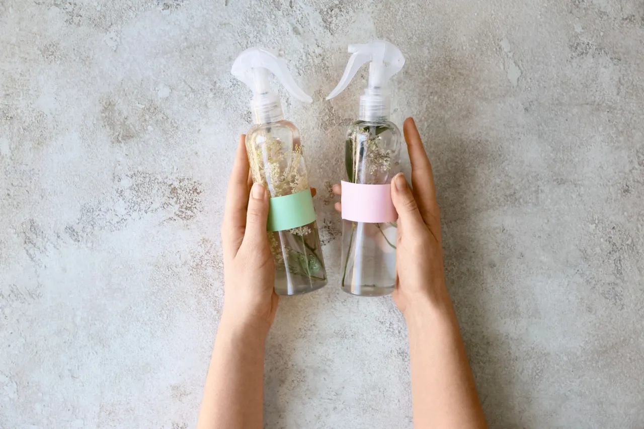 Dwie butelki z domowym zapachem do łazienki, wypełnione wodą i kwiatami. Proste i naturalne rozwiązanie, jak zrobić domowy zapach do łazienki.