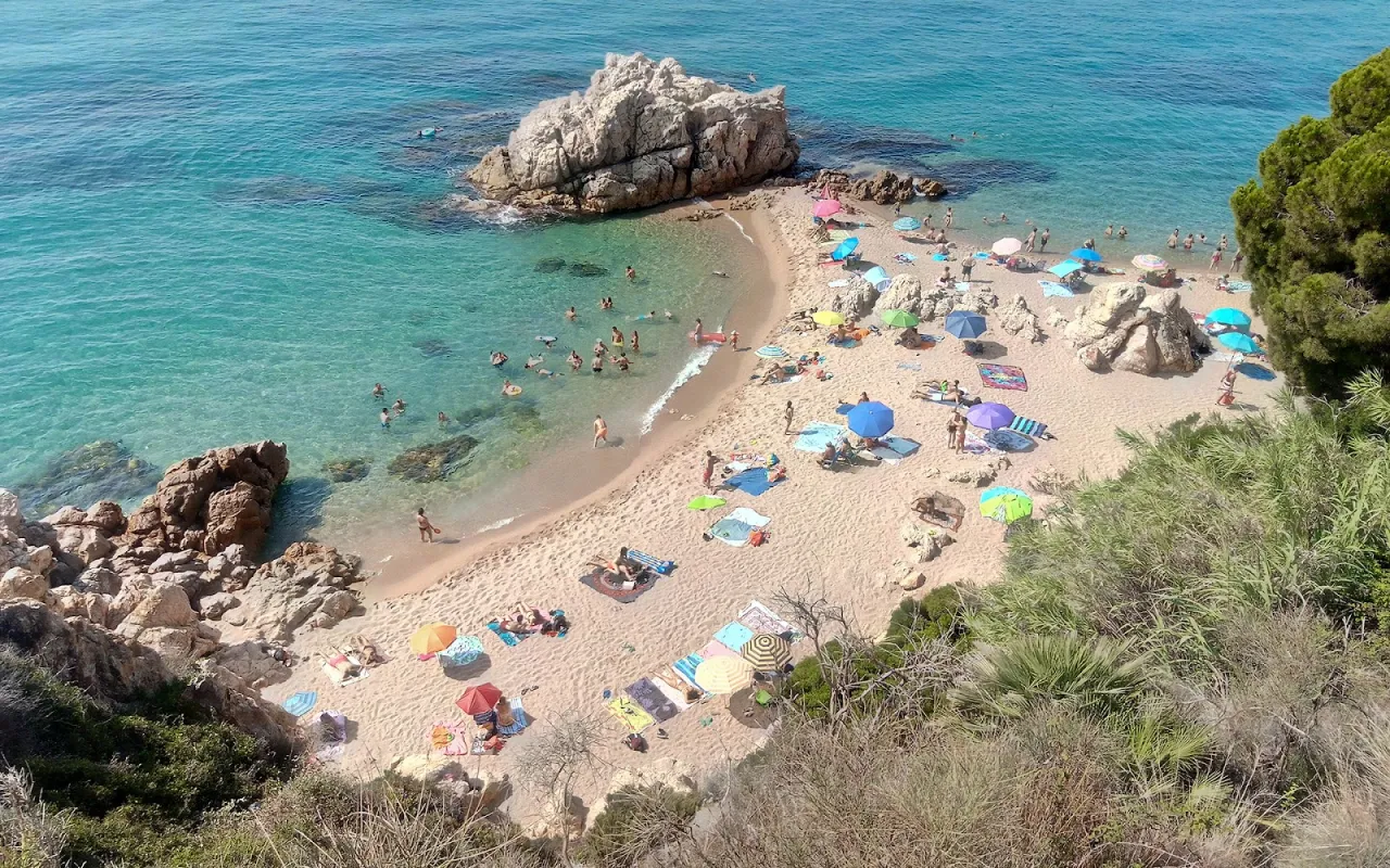 Piękna plaża z turkusową wodą i ludźmi relaksującymi się pod parasolami. To właśnie co można zobaczyć w Hiszpanii.