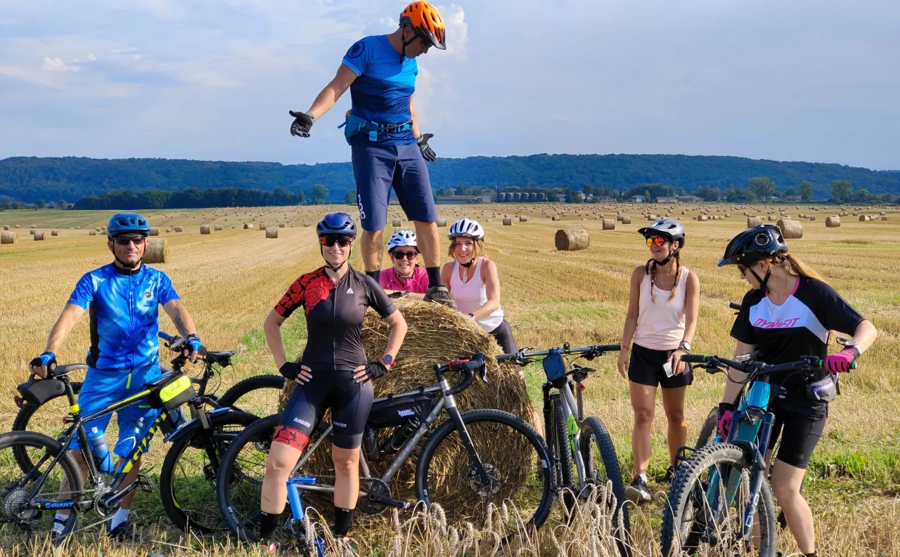 Grupa rowerzyst&oacute;w na tle p&oacute;l ze słomą, gotowa do podboju trasy rowerowej Szlak Orlich Gniazd.
