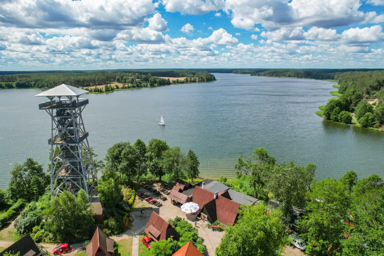 Wieża widokowa nad jeziorem, idealne miejsce, by zobaczyć, co warto zobaczyć na Kaszubach. Żaglówka na wodzie, las i błękitne niebo.