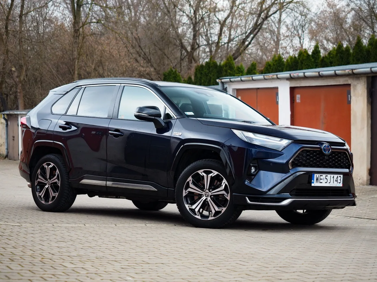 Ciemnoniebieska Toyota RAV4 Hybrid stoi na kostce brukowej. Zastanawiasz się, ile pali Toyota RAV4 Hybrid? Ten model oferuje niskie spalanie.