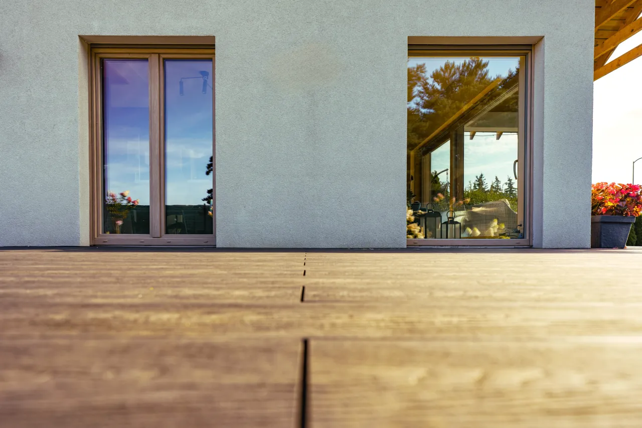 Nowoczesne okna z drewnianymi ramami odbijają niebo i zieleń. Czy okna dwukolorowe są droższe? To pytanie, na które warto poznać odpowiedź.