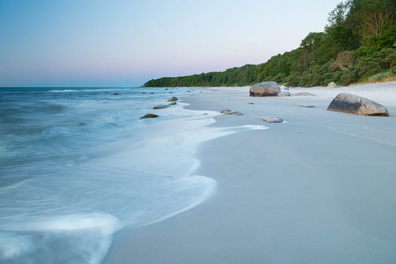 Spokojna plaża nad Bałtykiem, z łagodnymi falami i kamieniami. To jedne z najpiękniejszych polskich plaż nad Bałtykiem.