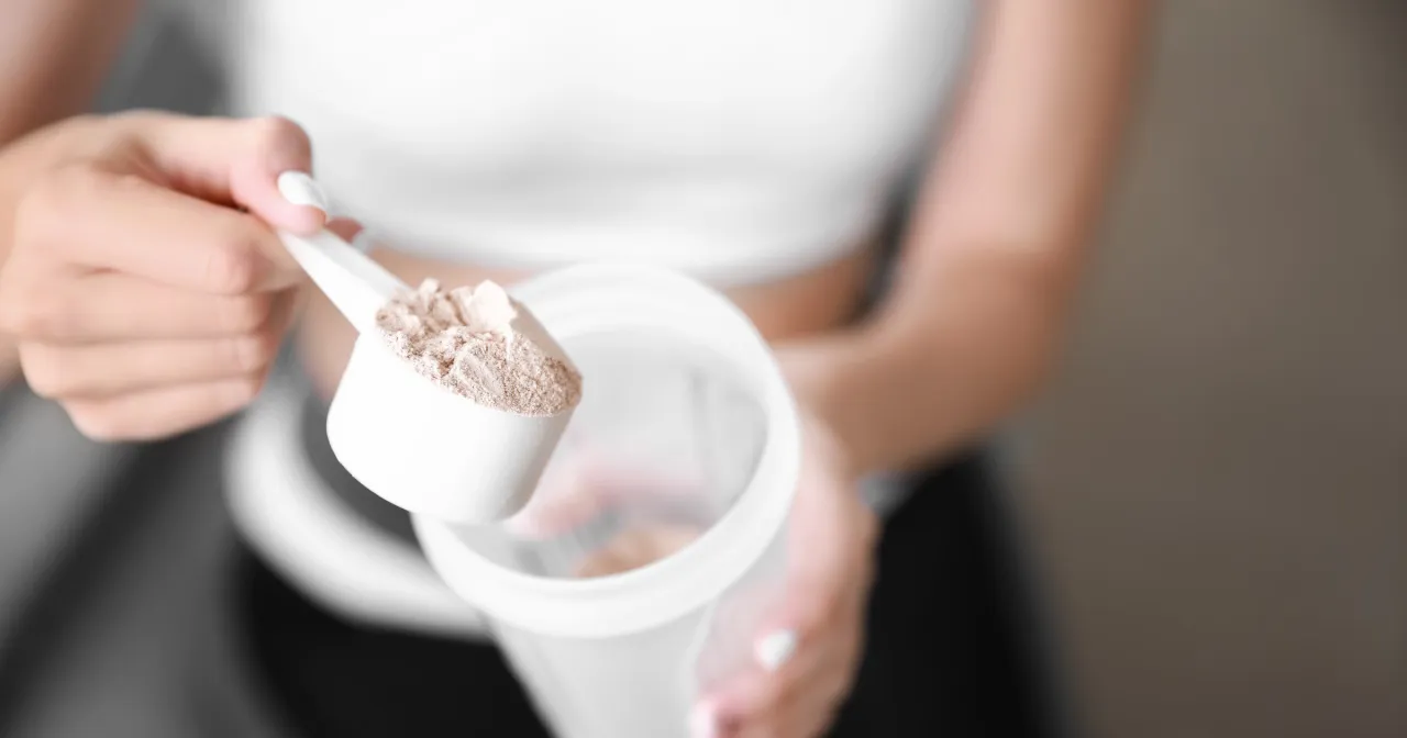 Kobieta dodaje proszek do shakera. Czy shake proteinowy jest zdrowy? To pytanie zadaje sobie wiele osób dbających o formę.