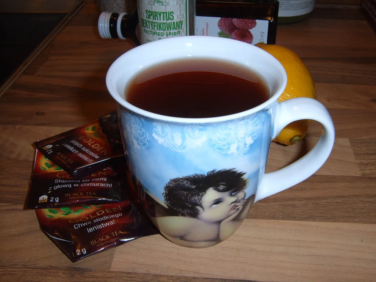 Kubek z herbatą, cytryna i saszetki czarnej herbaty. Idealne składniki, by dowiedzieć się, jak zrobić herbatę malinową.