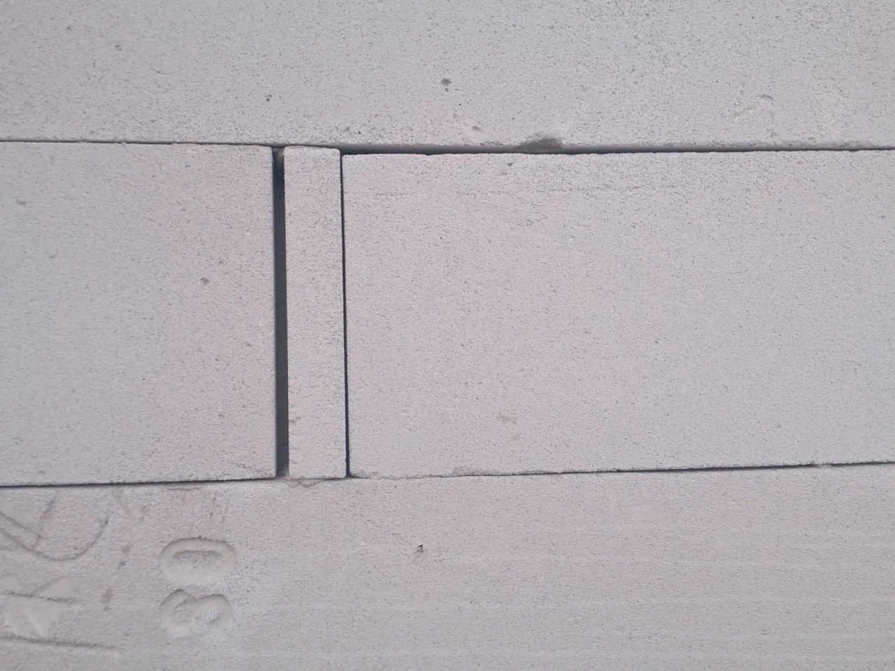 Zbliżenie na białe pustaki, gotowe do murowania ścianek działowych. Widoczne fugi i oznaczenie 