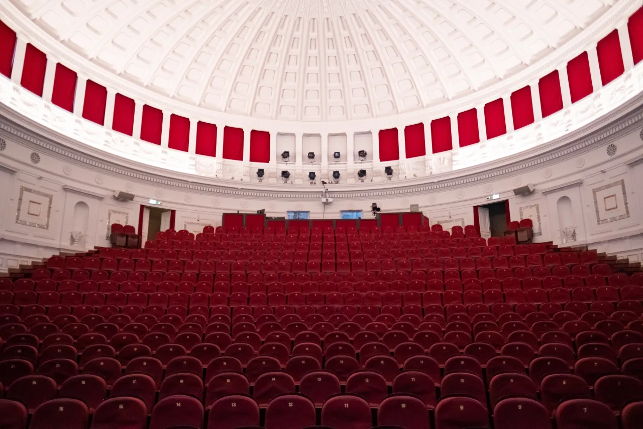 Puste czerwone fotele teatralne czekają na widzów najlepszych spektakli komediowych. Wnętrze z kopułą i czerwonymi zasłonami.