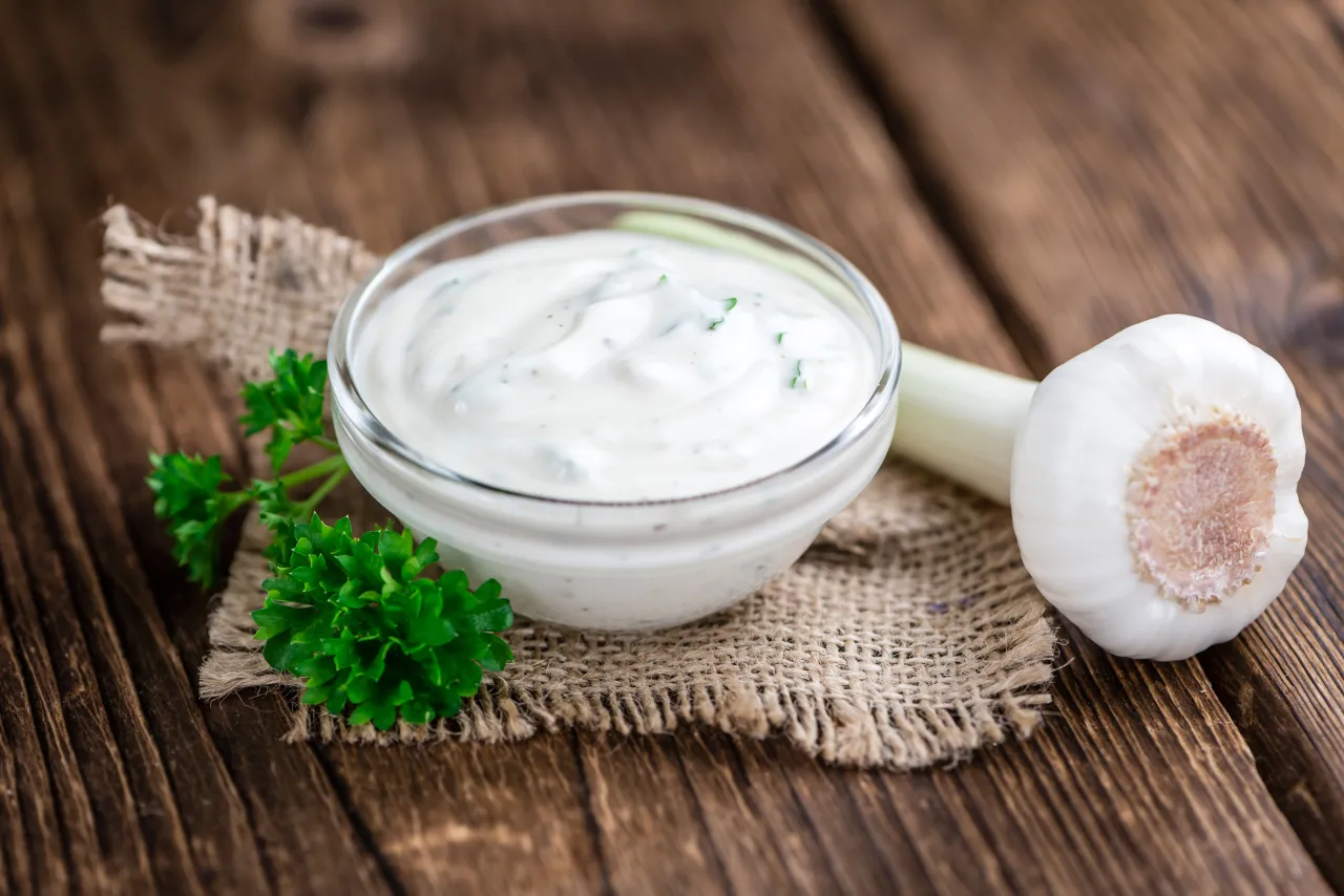 Aksamitny sos czosnkowy jak z restauracji, z czosnkiem i natką pietruszki, na drewnianym tle.