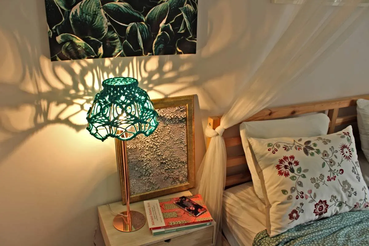 Ozdobny, zielony abażur do lampki nocnej jak zrobić. Wzory makramy rzucają cień na ścianę.