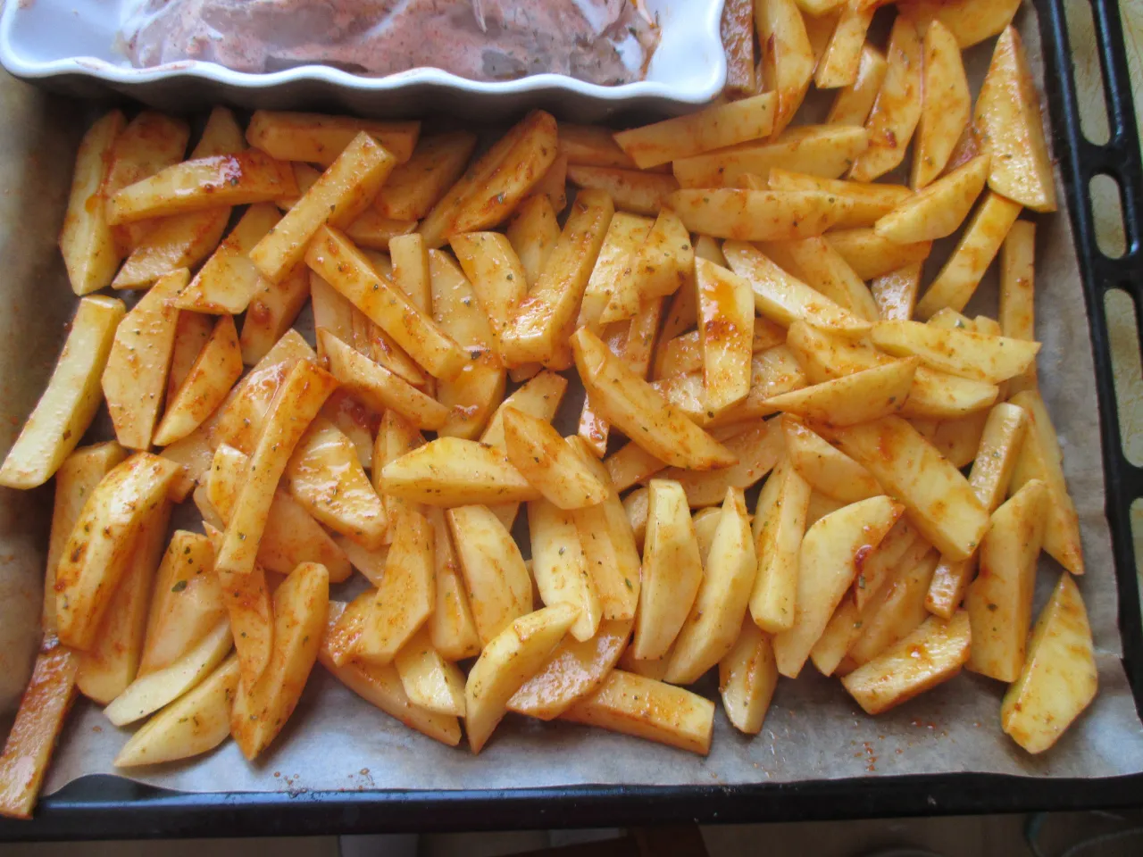 Gotowe do pieczenia frytki z ziemniak&oacute;w, przyprawione i ułożone na blasze. Idealne, by dowiedzieć się, jak zrobić frytki w piekarniku.