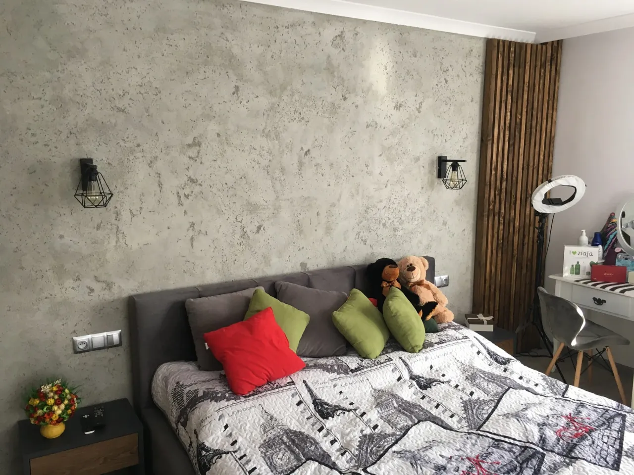 Ściana z efektem betonu dekoracyjnego, idealna inspiracja jak zrobić beton dekoracyjny. Łóżko z poduszkami i pluszakami.