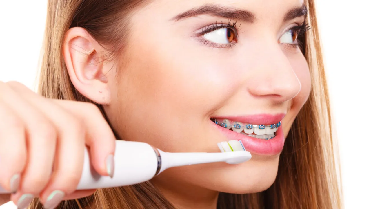 osoba z aparatem ortodontycznym myjąca zęby szczoteczką soniczną
