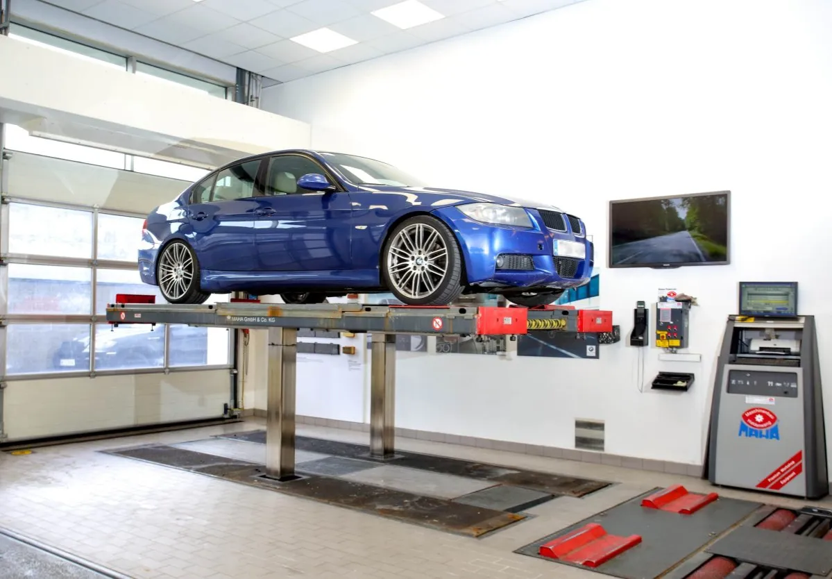 Niebieski sedan na podnośniku w warsztacie. W tle ekran z drogą, komputer i urządzenia diagnostyczne. Idealne miejsce, by dowiedzieć się, jak zwiększyć prześwit w samochodzie.