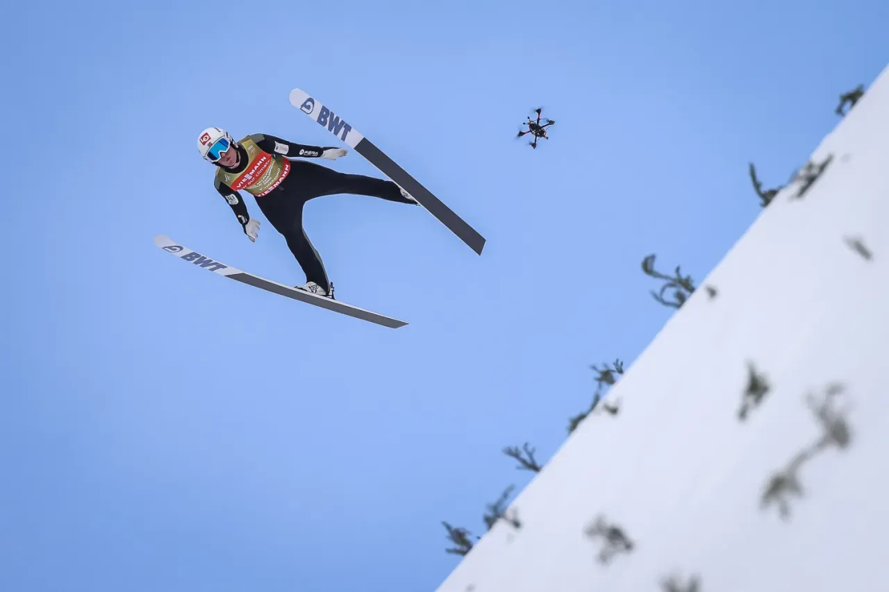 Skoczek narciarski w locie, a obok dron. Zastanawiasz się, ile ważą narty skoczków, które pozwalają na tak długie loty?