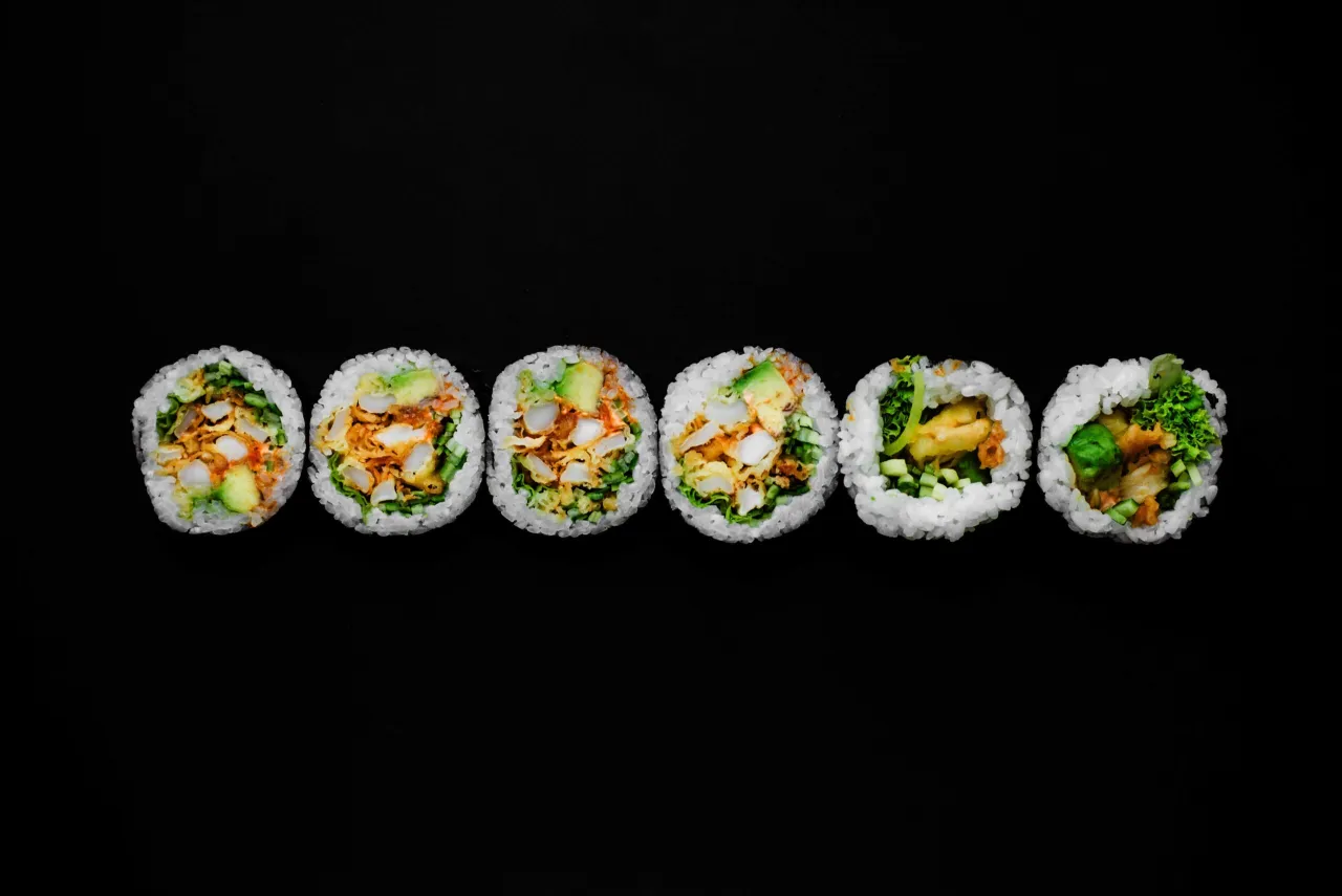 Sześć kawałków futomaki z awokado, kurczakiem i warzywami na czarnym tle.