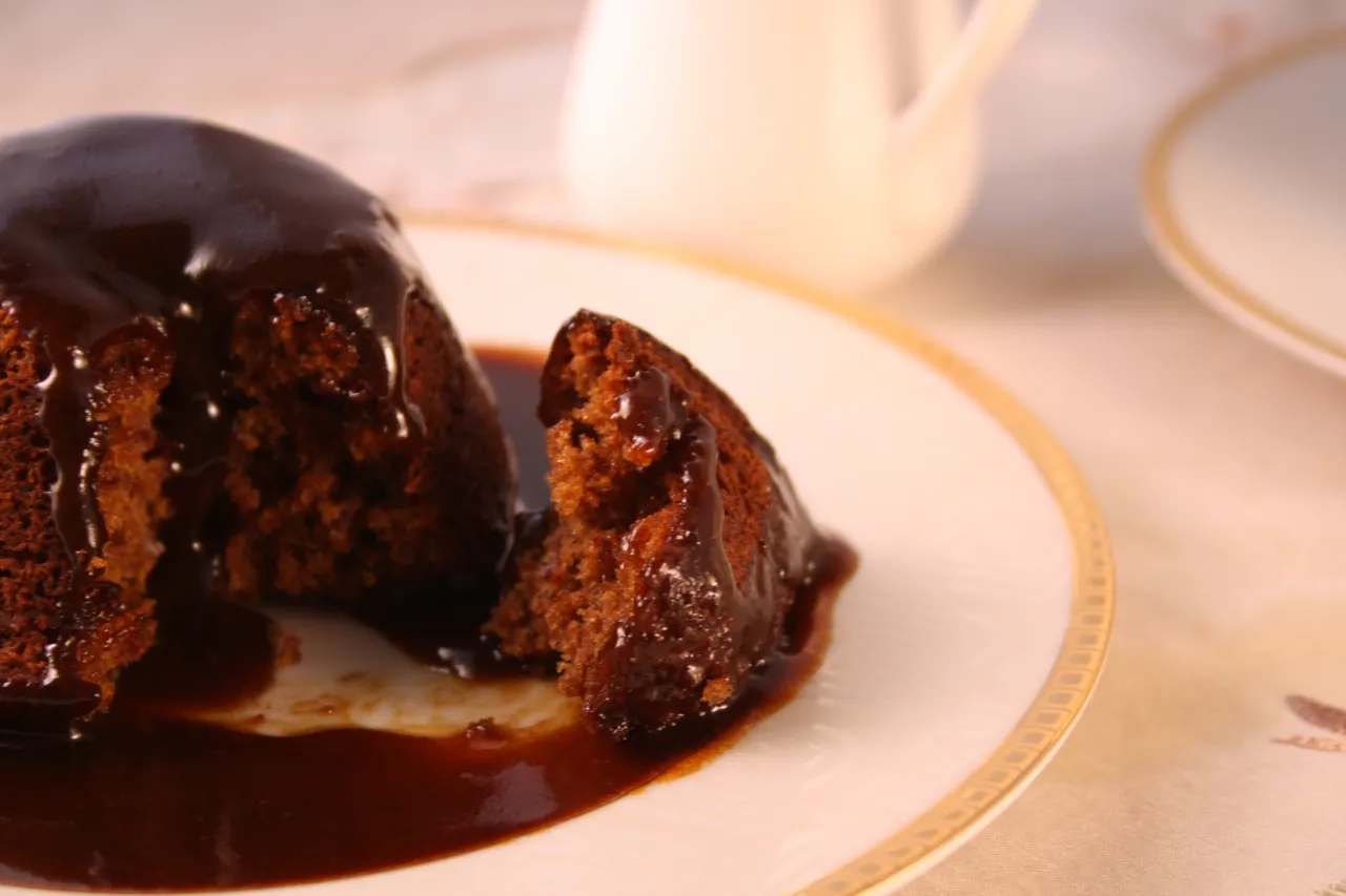Pyszny Sticky Toffee Pudding przepis. Czekoladowy deser polany sosem toffee na talerzu.