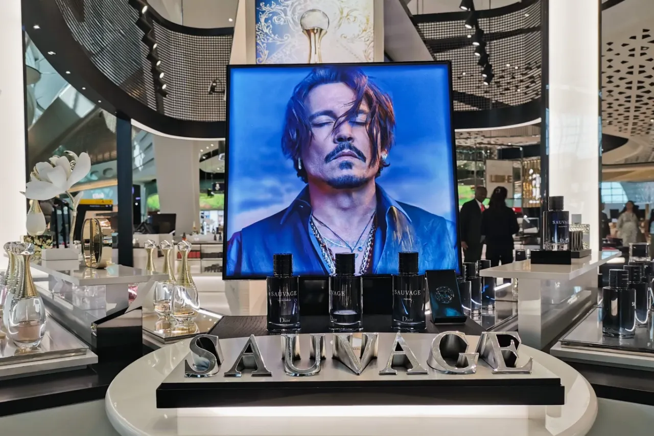 Osoba zastanawiająca się nad wyborem perfum, z dymkiem myślowym i znakiem zapytania