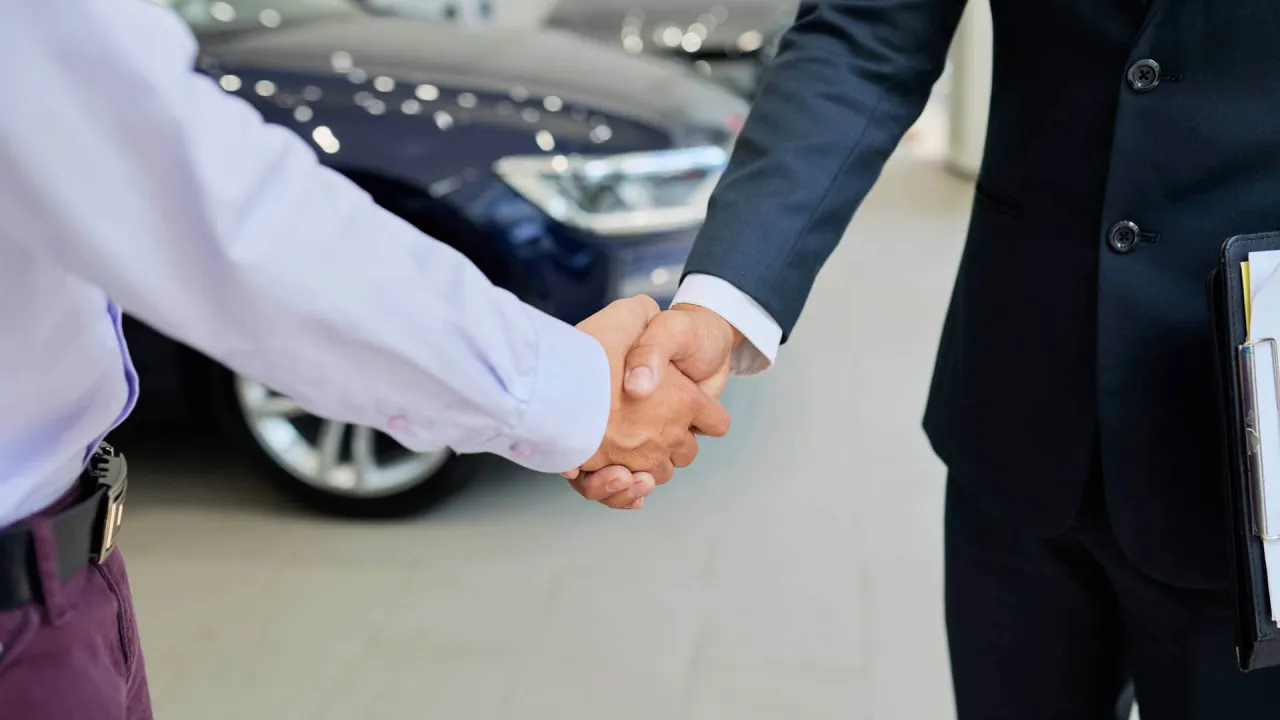 Uścisk dłoni między sprzedawcą a klientem przed nowym samochodem. Dowiedz się, jak sprzedać auto w leasingu.