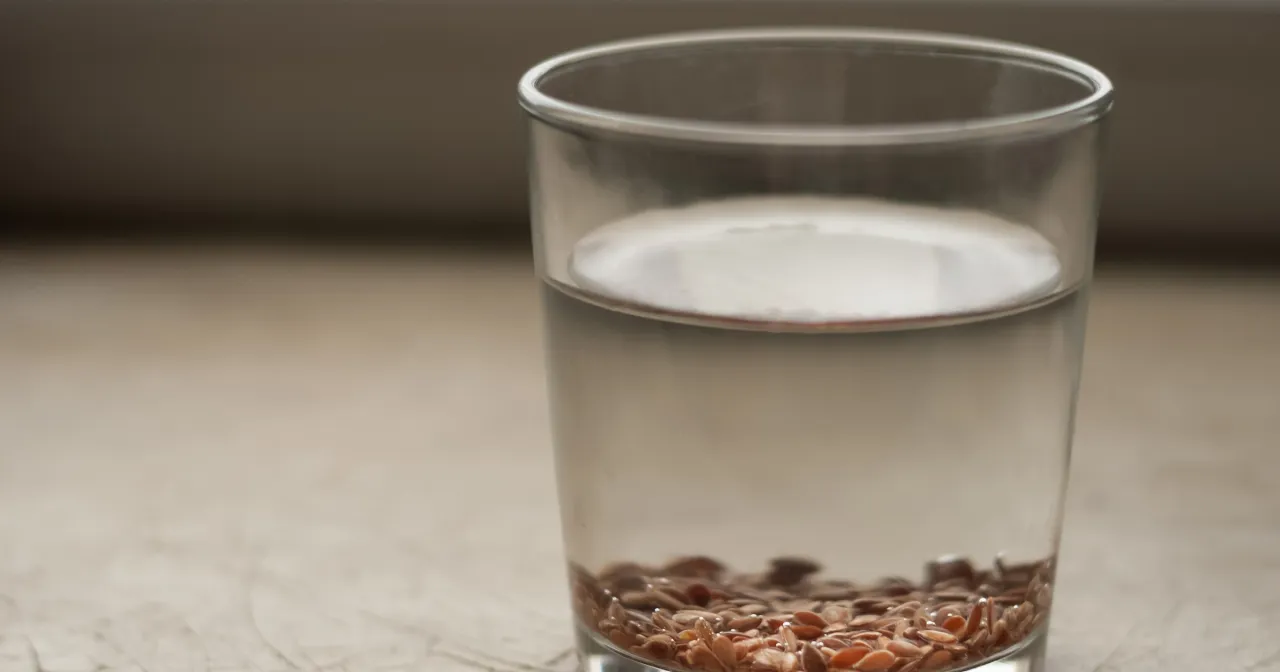 Szklanka z wodą i siemieniem lnianym. Czy od siemienia lnianego się tyje? Woda z nasionami lnu na stole.