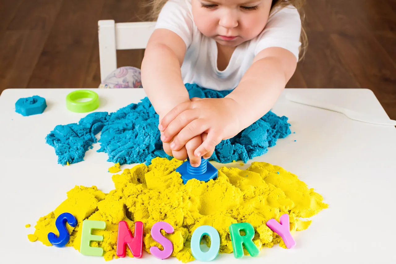 Dziecko bawi się masą sensoryczną, tworząc litery. To świetny sposób, jak pomóc dziecku z zaburzeniami sensorycznymi.